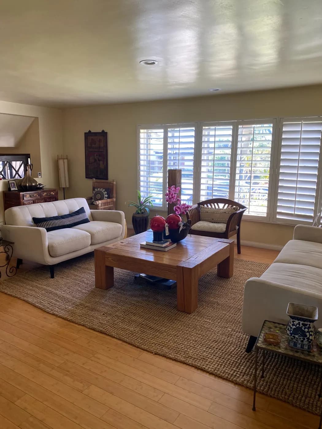 Residential living room with light seating, hardwood floors, and plantation shutters